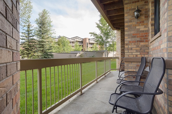 A private outdoor balcony awaits with two comfortable mesh lounge chairs overlooking lush green lawns and mature trees, perfect for your morning coffee or evening relaxation.