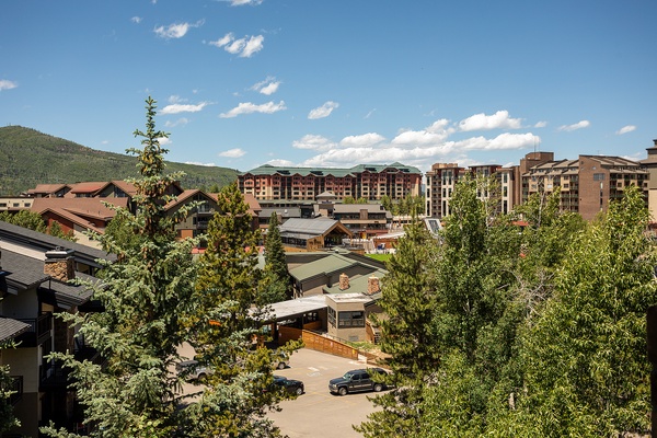 Mountain resort community nestled in a scenic valley with multi-story buildings, lush greenery, and dramatic peaks framing the village skyline.