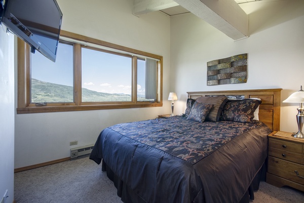 Wake up to stunning mountain vistas framed by large windows. Your cozy bedroom features plush bedding, warm wood furnishings, and peaceful views that make every morning special.