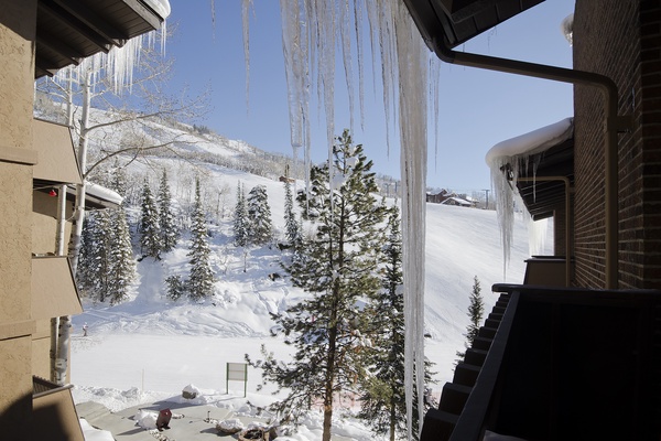 Stunning ski resort setting framed by dramatic icicles, with snow-covered slopes and frosted evergreens nestled at the base of pristine mountain peaks.