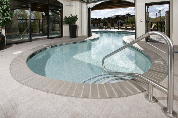 This inviting indoor-outdoor pool features a seamless flow connecting interior and exterior spaces, complete with spacious lounging areas and serene mountain views in the surrounding landscape.