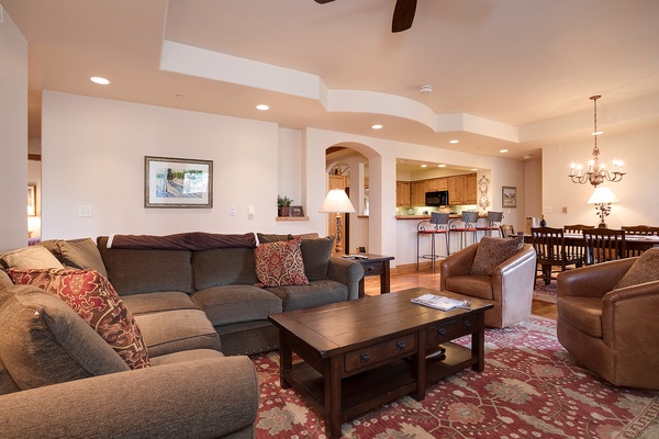 Settle into this spacious living room where plush sofas invite relaxation, warm lighting creates a cozy ambiance, and the open layout connects seamlessly to a full kitchen and elegant dining area—perfect for gathering with loved ones.