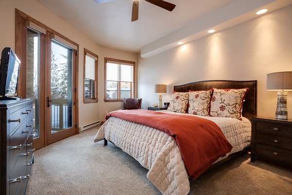 Unwind in your serene bedroom featuring a plush bed with elegant linens, warm lighting, and a private balcony door framing peaceful winter views for ultimate relaxation.