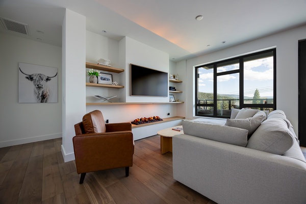 Sink into your cozy living room where a modern fireplace warms the space, and expansive windows frame the surrounding landscape. Unwind with your favorite shows or simply take in the peaceful setting just outside.