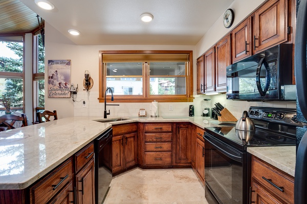 Your fully equipped kitchen features rich wood cabinetry, granite counters, and modern black appliances—perfect for preparing hearty mountain meals after a day exploring Steamboat Springs.