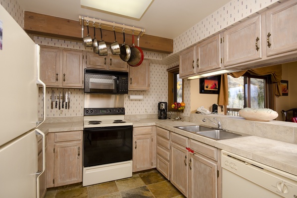 You'll love preparing meals in this fully equipped kitchen, where pots and pans hang within easy reach, bright counters offer plenty of space, and natural light pours in through the window.