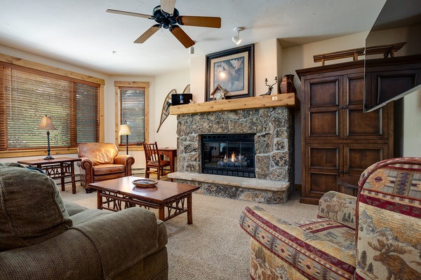 Unwind in your cozy living room with a crackling stone fireplace, comfortable seating, and warm wood furnishings perfect for mountain getaways.