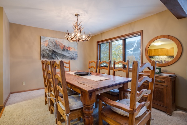 Gather around this rustic dining table with mountain views just beyond your window. The antler chandelier and warm wood tones create a cozy alpine atmosphere perfect for memorable meals together.