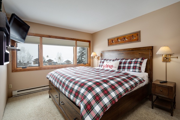 Drift off in your cozy bedroom with mountain views, warm plaid bedding, and thoughtful touches like bedside reading lamps and a wall-mounted TV for relaxed evenings.