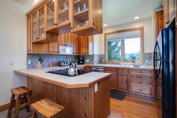 Your fully-equipped kitchen features warm wood cabinetry, modern appliances, and a breakfast bar for casual dining, all framed by stunning mountain vistas through the window.