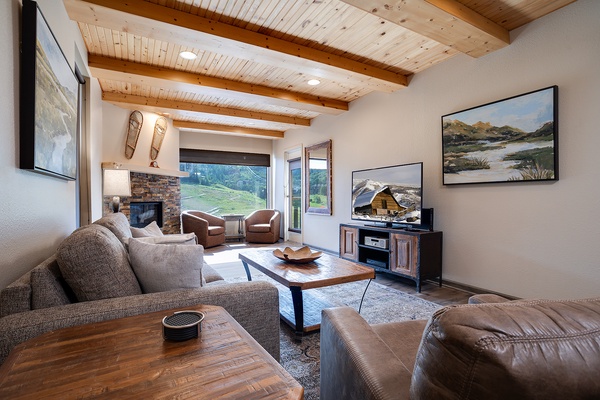 Unwind in your spacious living room, where exposed beam ceilings and a cozy stone fireplace create a mountain retreat atmosphere. Sink into plush seating while enjoying scenic views through expansive windows.