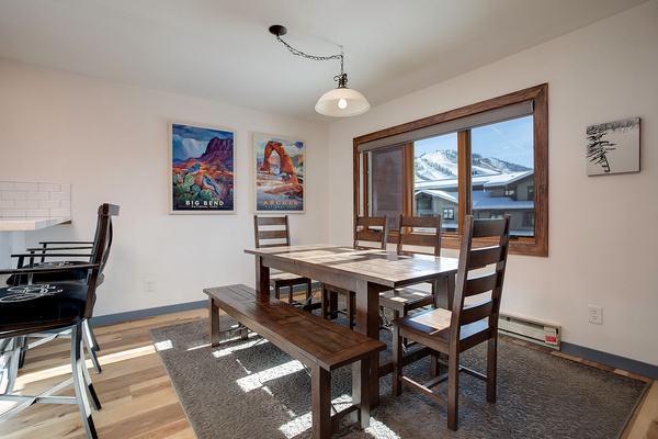 Gather around this inviting dining table where sunlight spills across warm wood floors. The mountain views through the window create a stunning backdrop for your morning coffee and shared meals.