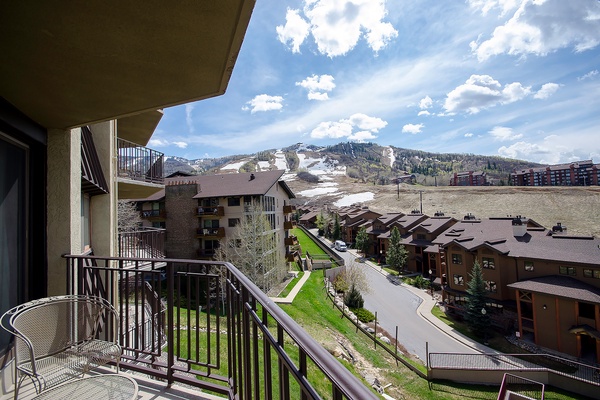A mountain resort community with ski slopes transitioning from winter, surrounded by residential buildings and natural landscape under partly cloudy skies.