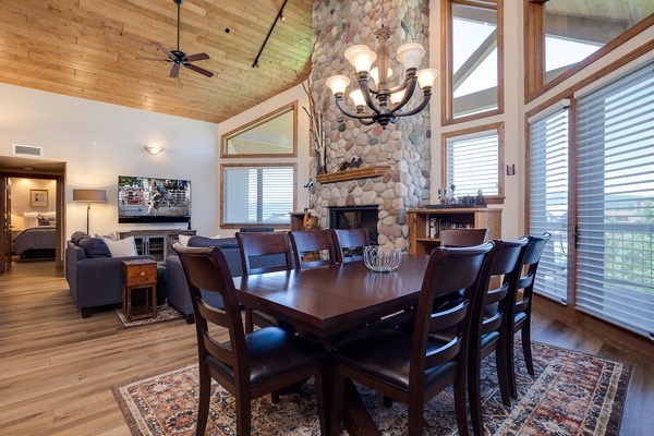 Gather around this handsome dining table beneath soaring wood ceilings and a river-stone fireplace. Natural light pours through floor-to-ceiling windows, framing views of the surrounding landscape while you share meals and make memories with loved ones.