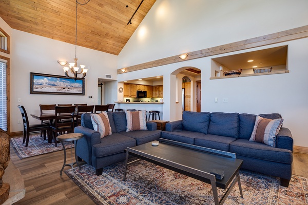 Unwind in this beautifully designed living space featuring a spacious sofa, cozy dining area, and fully equipped kitchen—all beneath stunning vaulted ceilings with warm wood accents that create your perfect mountain retreat.