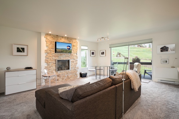 Unwind in your bright living room with cozy seating, a warm stone fireplace, and sliding doors that open to peaceful countryside views—perfect for relaxing after exploring nearby.