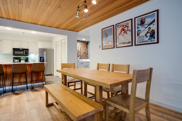 Gather around this inviting dining table for meals and memories, where warm wood tones, vintage ski posters, and a fully equipped kitchen create your perfect mountain retreat.
