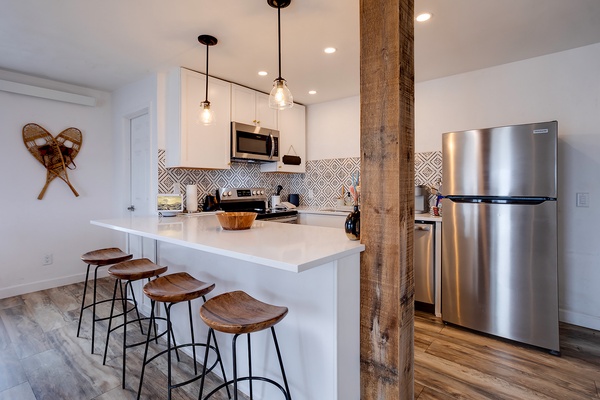 Your open kitchen features modern stainless appliances, sleek white counters, and a charming breakfast bar where you can sip morning coffee beneath warm pendant lights.