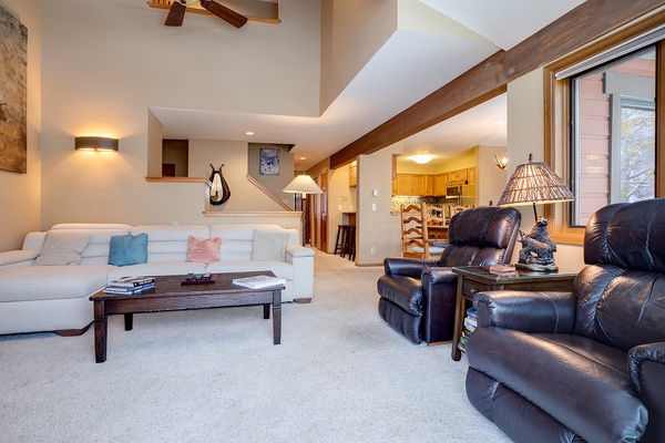 Unwind in your spacious living room where vaulted ceilings with warm wood beams, plush seating, and soft lighting create an inviting retreat after a day of mountain adventure.