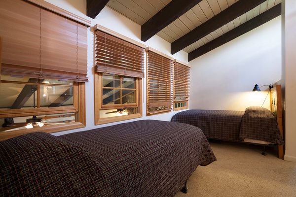 Unwind in your cozy retreat beneath exposed beam ceilings. Two comfortable beds invite restful sleep while warm lighting and wooden blinds create a peaceful mountain escape.