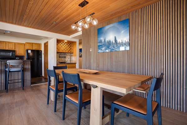 Gather around this handsome wood table beneath a warm plank ceiling and modern pendant lighting—your mountain retreat awaits, with a cozy kitchen just steps away for easy entertaining.