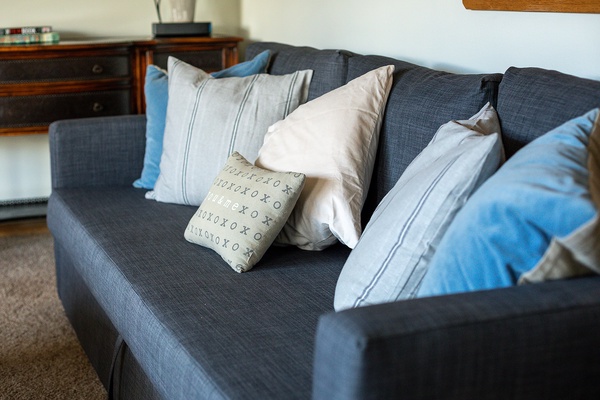 Sink into the plush charcoal sofa piled with soft pillows in calming blues and creams—your perfect spot to unwind with a book or morning coffee.