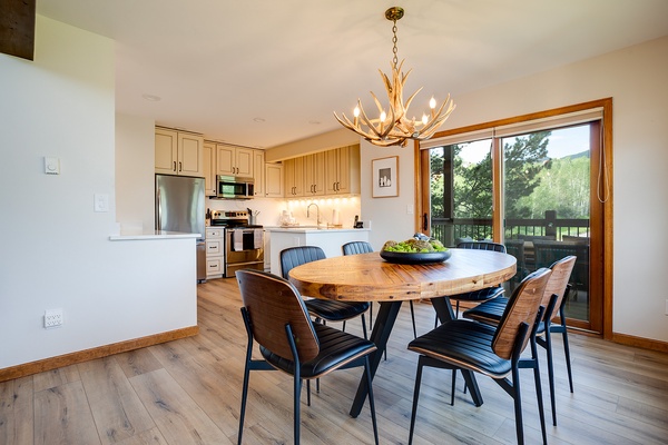 Gather around this inviting round table beneath a stunning antler chandelier, with natural light streaming through doors to your private balcony overlooking green landscapes.