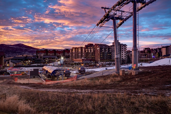 A mountain resort village at dusk, featuring ski lift infrastructure and multi-story lodging buildings set against a dramatic pink and purple sunset sky.