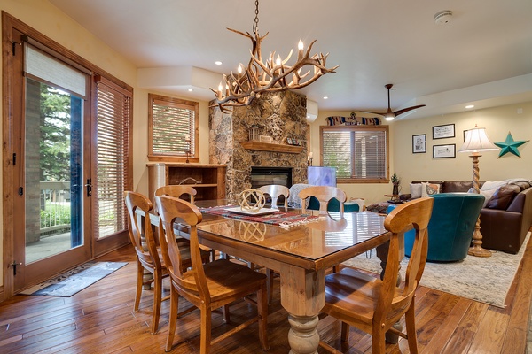 Gather around the rustic dining table under the antler chandelier, where warm wooden tones and a stone fireplace create a cozy mountain retreat for your meals and memories together.