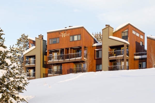 Modern alpine property with warm wood siding nestled on a snowy hillside, featuring multiple balconies and mountain-view access.