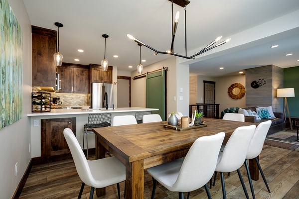 Gather around the rustic dining table, where warm wood tones and modern lighting create the perfect space for your meals and conversations, flowing seamlessly into your fully-equipped kitchen and cozy bedroom beyond.