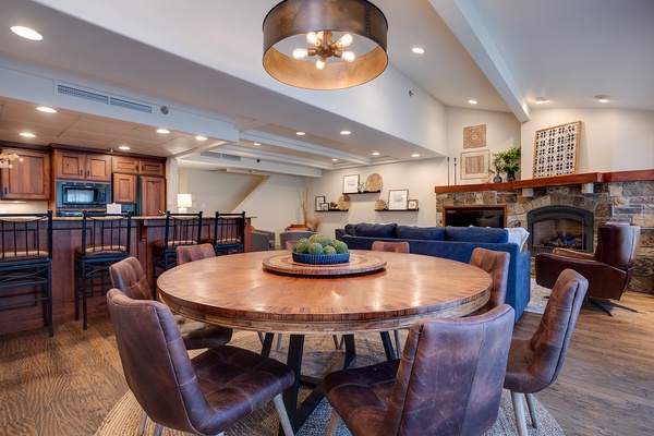 Gather around the stunning round dining table, perfect for lively meals and conversation. Beyond, sink into plush seating by the stone fireplace, where warmth and elegance meet.