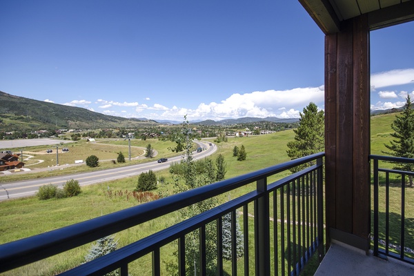 A scenic mountain valley panorama stretches across rolling green meadows and distant ridges under open blue skies, visible from the property's elevated position.