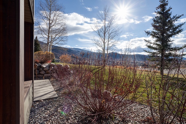 Stunning mountain views frame this vacation rental, with layers of dramatic peaks rising beyond open fields and bare deciduous trees in the foreground—a scenic mountain-side setting.