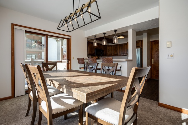 Gather around this rustic dining table where sunlight streams through large windows. The open layout flows seamlessly into a fully equipped kitchen with bar seating, perfect for your group meals and morning coffee.