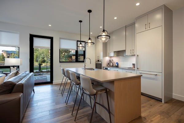 Your sleek modern kitchen invites you to gather around the spacious island, where pendant lighting illuminates a bright space designed for cooking and connection. Natural light streams through glass doors, opening your culinary hub to the outdoors.