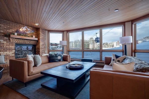 Relax in your mountain-view living room with plush leather seating, a warm fireplace, and floor-to-ceiling windows overlooking the slopes and ski gondola—your perfect alpine retreat.