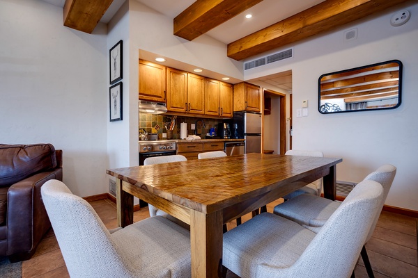 Gather around the handcrafted wood table beneath exposed timber beams. Your fully equipped kitchen awaits with stainless appliances, warm wood cabinetry, and open-concept flow perfect for meals together.
