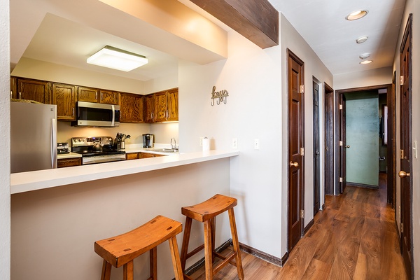 Your open kitchen with breakfast bar and rustic wood stools invites easy mornings, while warm beam accents and natural wood details add a cozy, inviting charm throughout.