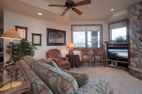 Settle into this warm living space with plush seating, a crackling stone fireplace, and large windows framing peaceful views—your perfect retreat for cozy evenings.