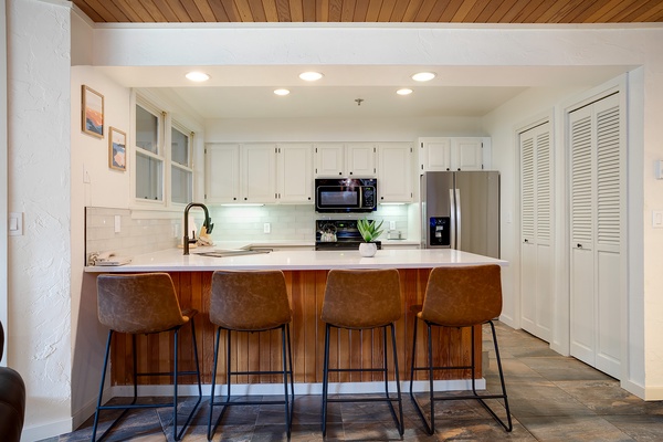 Gather around your bright, modern kitchen where clean lines meet warm wood tones. Four barstools invite you to linger over morning coffee or evening cocktails at the spacious island.