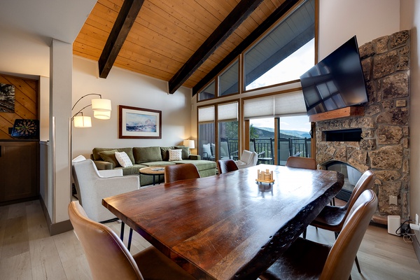 Gather around the handsome wood table or relax on the plush sofa—your mountain retreat combines rustic stone and warm beams with sweeping vistas through floor-to-ceiling windows.