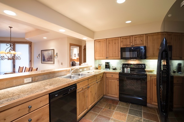 Your fully equipped kitchen features granite counters, warm wood cabinetry, and modern black appliances—perfect for preparing home-cooked meals with everyone gathered around.