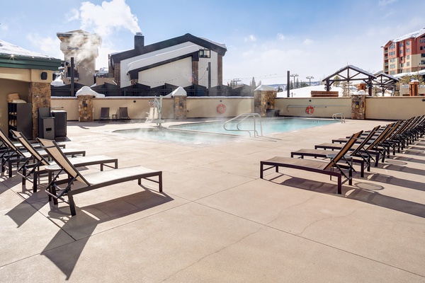 A heated outdoor pool surrounded by sun loungers offers a perfect relaxation spot. Stone columns and mountain views complete this inviting winter retreat.