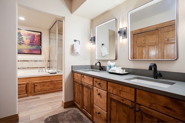 Step into your private retreat with a spacious dual-sink vanity and a soaking tub just beyond. Warm wood tones and modern fixtures create a perfect blend of rustic charm and comfort.