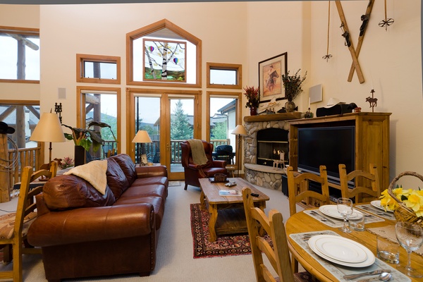 Sink into plush leather sofas as natural light floods through soaring windows, framing mountain views. Warm your evenings by the stone fireplace, gather around the rustic dining table, and let the cozy lodge atmosphere make you feel right at home.