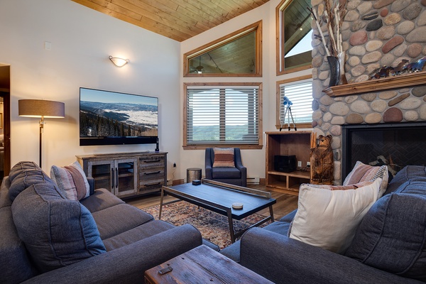Sink into plush couches, warm your toes by the stone fireplace, and watch mountain vistas on the big screen—your cozy alpine retreat awaits with vaulted wood ceilings and rustic charm.