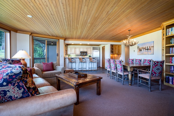 Relax in this spacious open-plan living area where rustic wood ceilings meet vibrant patterned accents. Your dining table awaits family meals, while plush seating invites cozy evenings.