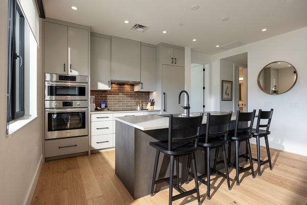 Your modern kitchen invites you to gather around the sleek island for morning coffee or casual meals, with gleaming stainless-steel appliances and warm wood floors underfoot.