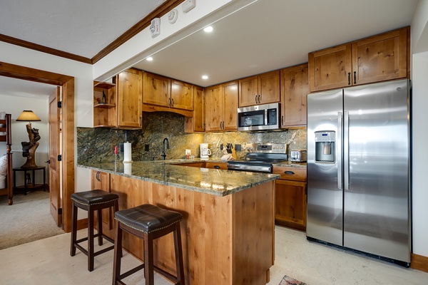 Your fully-equipped kitchen features rich wood cabinetry, gleaming granite counters, stainless steel appliances, and a breakfast bar perfect for morning coffee or casual meals.
